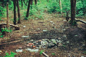 Garbage pile in forest among plants. Toxic plastic into nature everywhere. Rubbish heap in park...