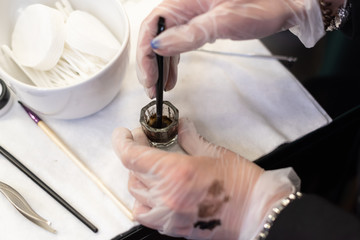 Beauty brows care concept: master is mixing henna for eyebrows coloring. swatches on hand in glove