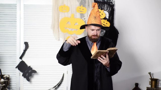 Magic, spell, book of magic. Bearded magician reads an old book about magic. Halloween Wizard. Magician reads a secret book on Halloween. Mystical professor. Fun creative education. Halloween hat.
