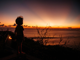 Fototapeta premium A boy in a helmet looks at the sunset at sea on the viewpoint