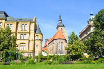 Franciscan Monastery and Church in Plzen, Czech Republic shot from green park in Krizikovy sady. Historical buildings, tourist attraction. Pilsen, Western Bohemia, Czechia. Sunny day, blue sky