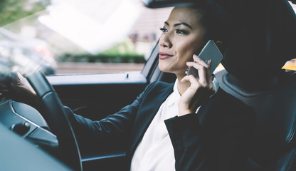 Professional female driver concentrated on road trip in automobile making international call conversation with colleague for discussing time of business meeting, woman trader using smartphone gadget