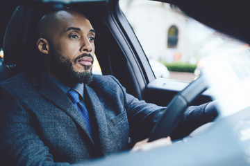 Bored male executive entrepreneur dressed in formal clothing driving to office destination feeling tired from long day in enterprise, serious man holding hands on steering wheel and looking on road