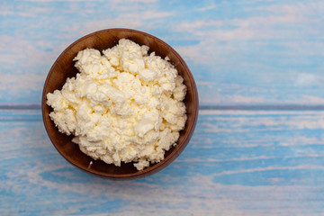 fresh cottage cheese in wooden bowl on blue wooden background