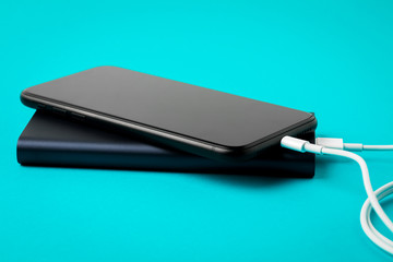 Smartphone charging with Power Bank via USB cable on blue background top view.