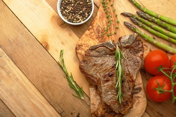 Marbled beef steak on a board with rosemary pepper, spices, and fresh vegetables on a wooden background, restaurant menu, gastronomy, tasty food. Horizontal photo, banner