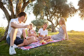 young happy family on a picnic in the summer in the park at sunset smiling drinking fruit juice