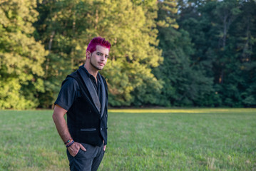 Alternative diverse male - black clothes, pink hair smirking at camera.