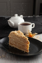 Slice of russian layered napoleon cake with vanilla cream filling and a cup of aroma black tea