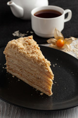 Slice of russian layered napoleon cake with vanilla cream filling and a cup of aroma black tea