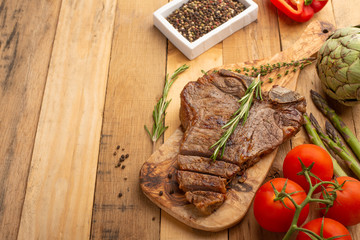 Marbled beef steak on a board with rosemary pepper, spices, and fresh vegetables, tomatoes and asparagus, artichoke, on a wooden background, restaurant menu, gastronomy, tasty food, restaurant service
