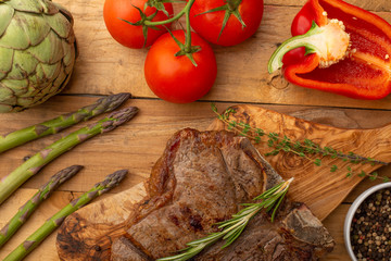 Marbled beef steak on a board with rosemary pepper, seasoning, and fresh vegetables on a wooden background, restaurant menu, gastronomy, tasty food. Restaurant service