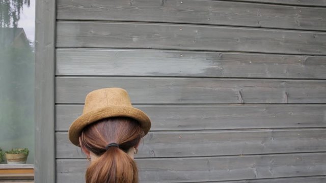 Woman worker painting wooden house exterior wall with paintbrush and wood protective color