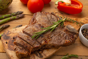 Marbled beef steak on a board with rosemary pepper, seasoning, and fresh vegetables on a wooden background, restaurant menu, gastronomy, tasty food. Restaurant service