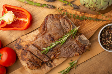 Marbled beef steak on a board with rosemary pepper, seasoning, and fresh vegetables on a wooden background, restaurant menu, gastronomy, tasty food. Restaurant service
