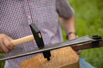 man knocking a scythe blade with hammer 