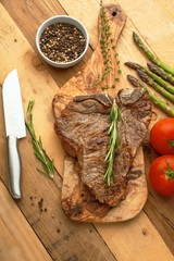 Marbled beef steak on a board with rosemary pepper, seasoning, and fresh vegetables on a wooden background, restaurant menu, gastronomy, tasty food. Restaurant service, verikalnoe photo, banner