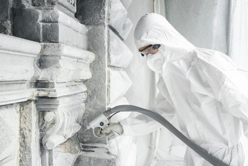 Man in a white protective uniform cleans stone carved sculpture from the dirt and concrete with a...