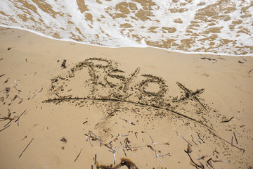 Summer holiday concept with relax word handwritten on the beach, in front of the waves