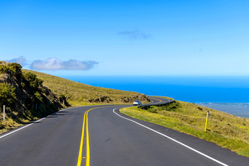 Haleakala Highway - A bright sunny day view of winding Haleakala Highway, against blue sky and blue Pacific Ocean. Haleakala National Park, Maui, Hawaii, USA.