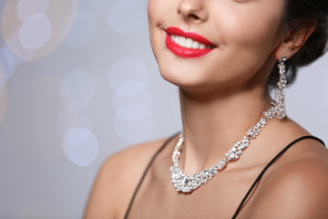 Beautiful woman with elegant jewelry on blurred background, closeup. Space for text