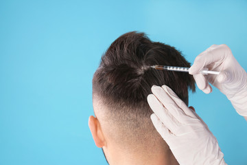 Young man with hair loss problem receiving injection on color background. Space for text