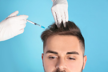 Young man with hair loss problem receiving injection on color background, closeup
