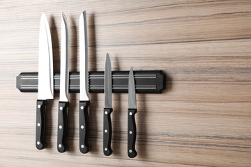 Magnetic holder with set of knives on wooden background. Space for text