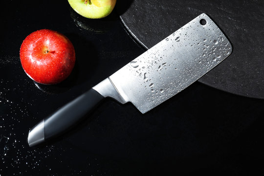 Cleaver and apples on wet black surface, flat lay