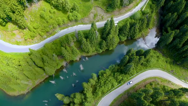 Aerial view of car driving through the fores and the lake on the side. Beautiful mountain road. Driving on the mountain road. Road trip. Mountain forest lake landscape. Car driving through pine forest