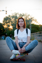Young woman sitting on the longboard at sunset