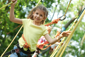 Little girl climbing in adventure park. Summer camp