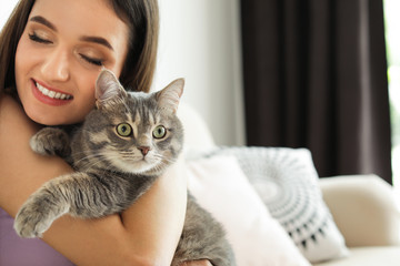 Young woman with cute cat at home, space for text. Pet and owner