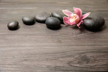 Fototapeta na wymiar Spa stones with orchid flower on wooden background. Space for text