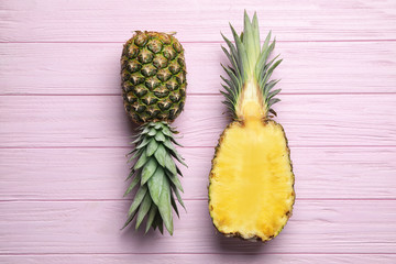 Fresh whole and cut pineapples on pink wooden background, top view