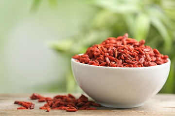 Bowl of dried goji berries on table against blurred background. Space for text