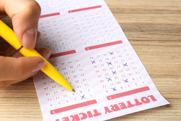 Woman filling out lottery ticket with pen on wooden table, closeup. Space for text