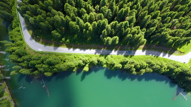 Aerial view of car driving through the fores and the lake on the side. Beautiful mountain road. Driving on the mountain road. Road trip. Mountain forest lake landscape. Car driving through pine forest