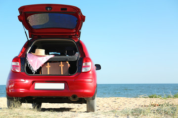 Fototapeta na wymiar Retro suitcase and beach accessories in car trunk on sand near sea. Space for text