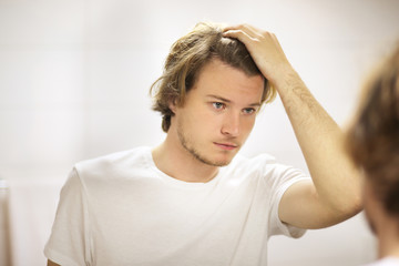 young man looking in the mirror,combing his hair,looking at problems on face