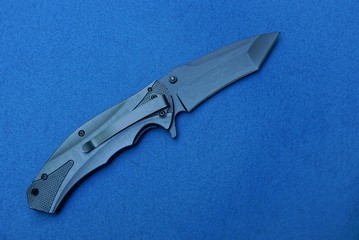  black metal military folding knife lies on a blue table