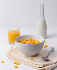 Corn flakes and glass of juice with bottle of milk at the white table.