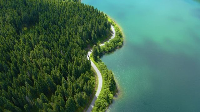 Aerial view of car driving through the fores and the lake on the side. Beautiful mountain road. Driving on the mountain road. Road trip. Mountain forest lake landscape. Car driving through pine forest