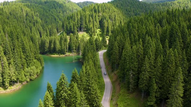 Mountain lake with turquoise water and green trees. Car driving through the forest and the lake on the side. Summer landscape with mountains, forest and lake. Aerial View over a mountain forest lake
