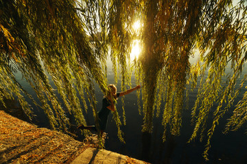 Autumn portrait of smiling young girl near willow on the background of a lake at sunset © Sergiy