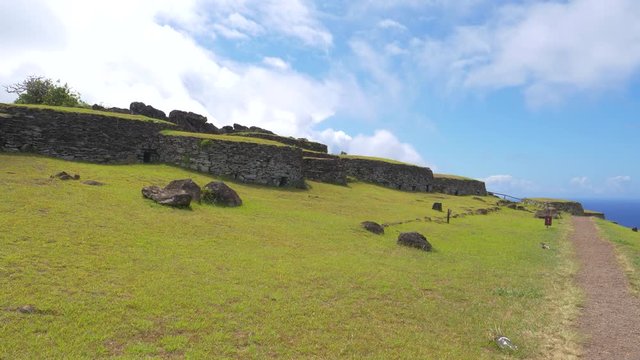 DRONE: Vacant path runs past a historic village with grass covered stone houses on exotic island. Flying above an empty trail leading past the village of Orongo. Old stone houses on Easter Island.