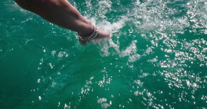 Slow motion of a female hand is touching a clear transparent water and enjoys the day at the sea alongside the waves of the boat. 