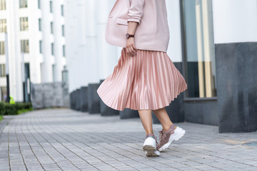Pleated skirt coral color and sneakers. The girl is very dynamic posing on the street, the skirt is developing.
