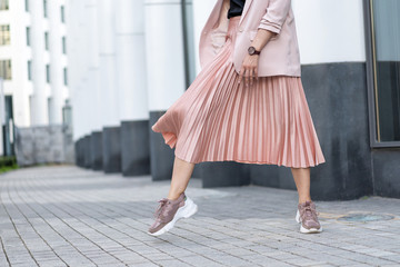 Pleated skirt coral color and sneakers. The girl is very dynamic posing on the street, the skirt is developing.