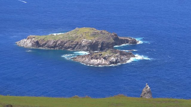CLOSE UP: Small ocean waves drift past the ancient islet of Motu Nui on a sunny summer day. Scenic view from above of small rocky islands used for bird man rituals near world famous Easter Island.